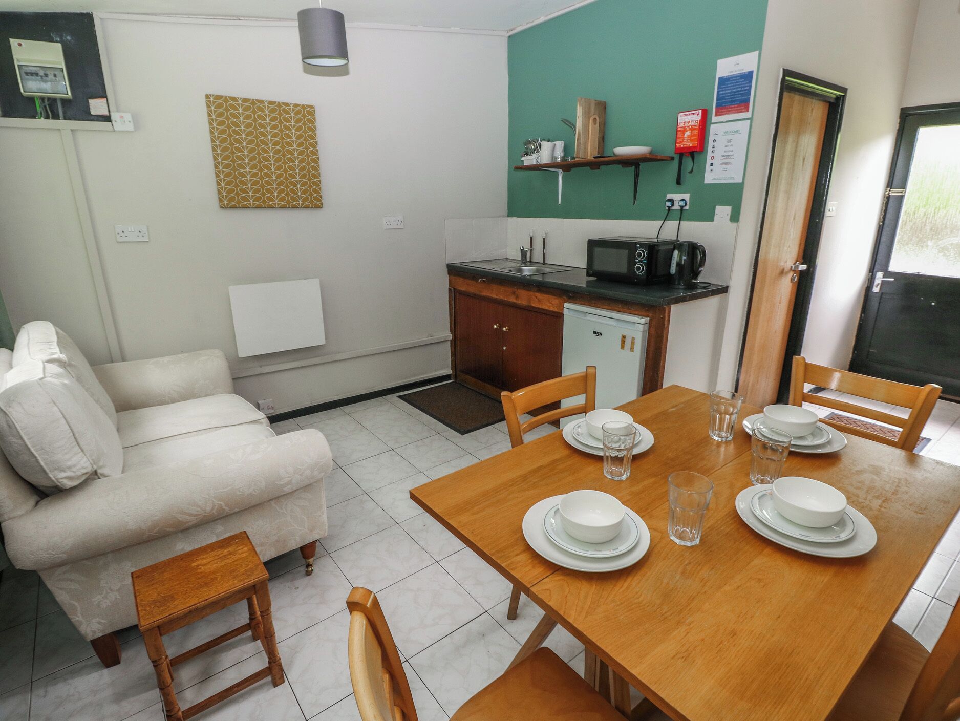 A compact living space with a dining table set for four, a sofa, a kitchenette, and a small refrigerator.