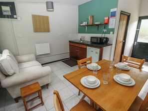 Un espacio habitable compacto con una mesa de comedor lista para cuatro personas, un sofá, una kitchenette y un refrigerador pequeño.