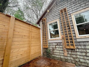 Eine Holzterrasse mit Holzlattenzaun, einer Leiter und einem Haus mit zwei Fenstern.