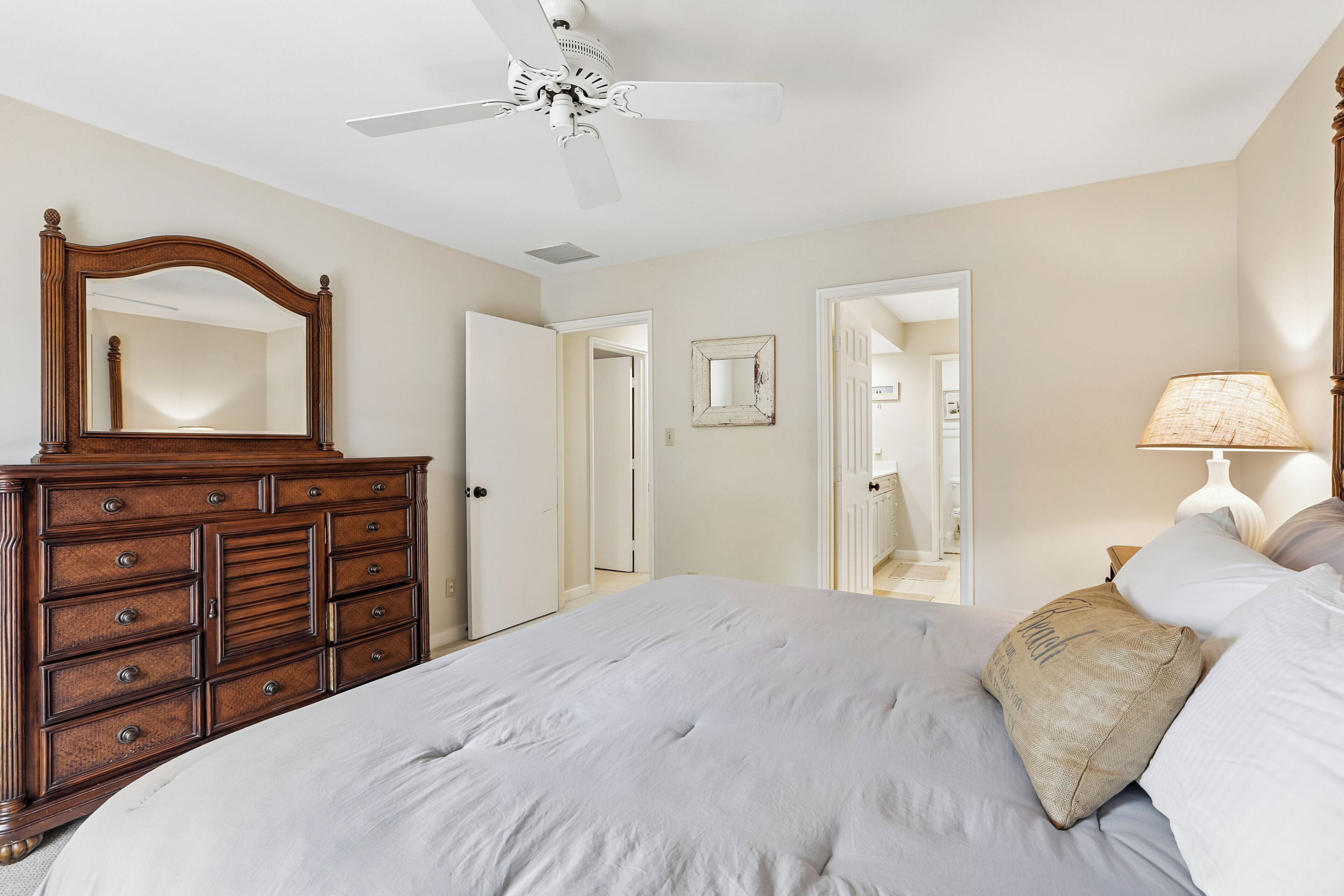 Un dormitorio con cama, cómoda, ventilador de techo y una puerta que da a otra habitación.