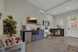 Un salon moderne avec un canapé gris, un coin repas doté d’un buffet bleu et une grande fenêtre avec des stores.