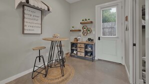 Eine Küche mit einem Holztisch, Hockern, einem sechseckigen Regal mit Pflanzen und einer Tür mit Fenster.