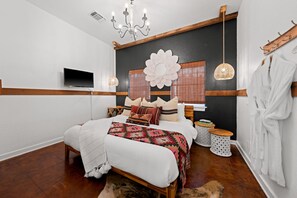 A bedroom with a large bed, a TV mounted on the wall, a chandelier, and a wooden headboard. - Poplar Place Main - Hot Tub & Fire Pit (Fredericksburg)