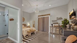 A modern bedroom with a glass shower, a bed with a bench, a coffee table, and a decorative mirror. - Poplar Place 3 - Hot Tub & Close to Downtown (Fredericksburg)