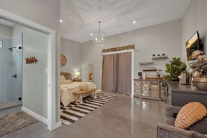 A modern bedroom with a glass shower, a bed with a bench, a coffee table, and a decorative mirror. - Poplar Place 3 - Hot Tub & Close to Downtown (Fredericksburg)