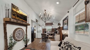 A spacious living room with a fireplace, a dining area, and a kitchen in the background. - Poplar Place Soho - Cozy Cottage with Hot tub (Fredericksburg)