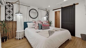 A bedroom with a bed, bedside tables, a mirror, curtains, a hanging lamp, and a sliding door. - Poplar Place Soho - Cozy Cottage with Hot tub (Fredericksburg)