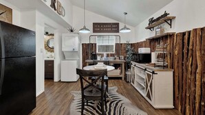 A modern kitchen with a refrigerator, white cabinets, a wooden dining table, and pendant lights. - Poplar Place Soho - Cozy Cottage with Hot tub (Fredericksburg)
