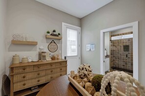 Ein Zimmer mit einem Holzkoffer, einem Fenster mit Jalousien, einem Wandbehang und einem raumgestaltenden Duschbereich.