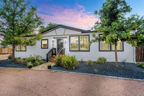 A single-story house with a front porch, a staircase leading to the entrance, and a well-maintained garden with various plants and shrubs. - Poplar Place Mod - Hot tub & Fire Pit (Fredericksburg)