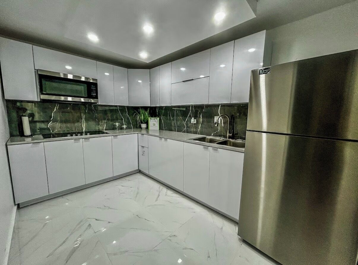 Uma cozinha moderna com armários brancos, geladeira de aço inoxidável, micro-ondas e painel de fundo de mármore.