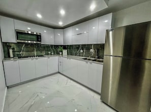 Eine moderne Küche mit weißen Schränken, einem Edelstahlkühlschrank, einer Mikrowelle und einer Marmor-Spritzschutzwand.