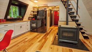 Eine moderne Küche mit Holzboden, einem roten Stuhl, einem schwarzen Kühlschrank und einem Kaminofen.