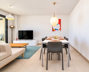 A modern living room with a sofa, a dining table set for four, a TV, and artwork on the wall. - Arenal Dream Glow Apartment Jávea (Javea / Xàbia)