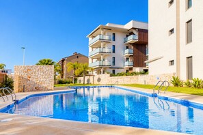A swimming pool with a stone wall and metal railings, surrounded by modern apartment buildings with balconies. - Arenal Dream Glow Apartment Jávea (Javea / Xàbia)