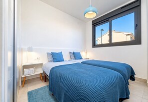 A bedroom with two beds, a window with a view, a bedside table with a lamp, and a blue rug. - Arenal Dream Glow Apartment Jávea (Javea / Xàbia)