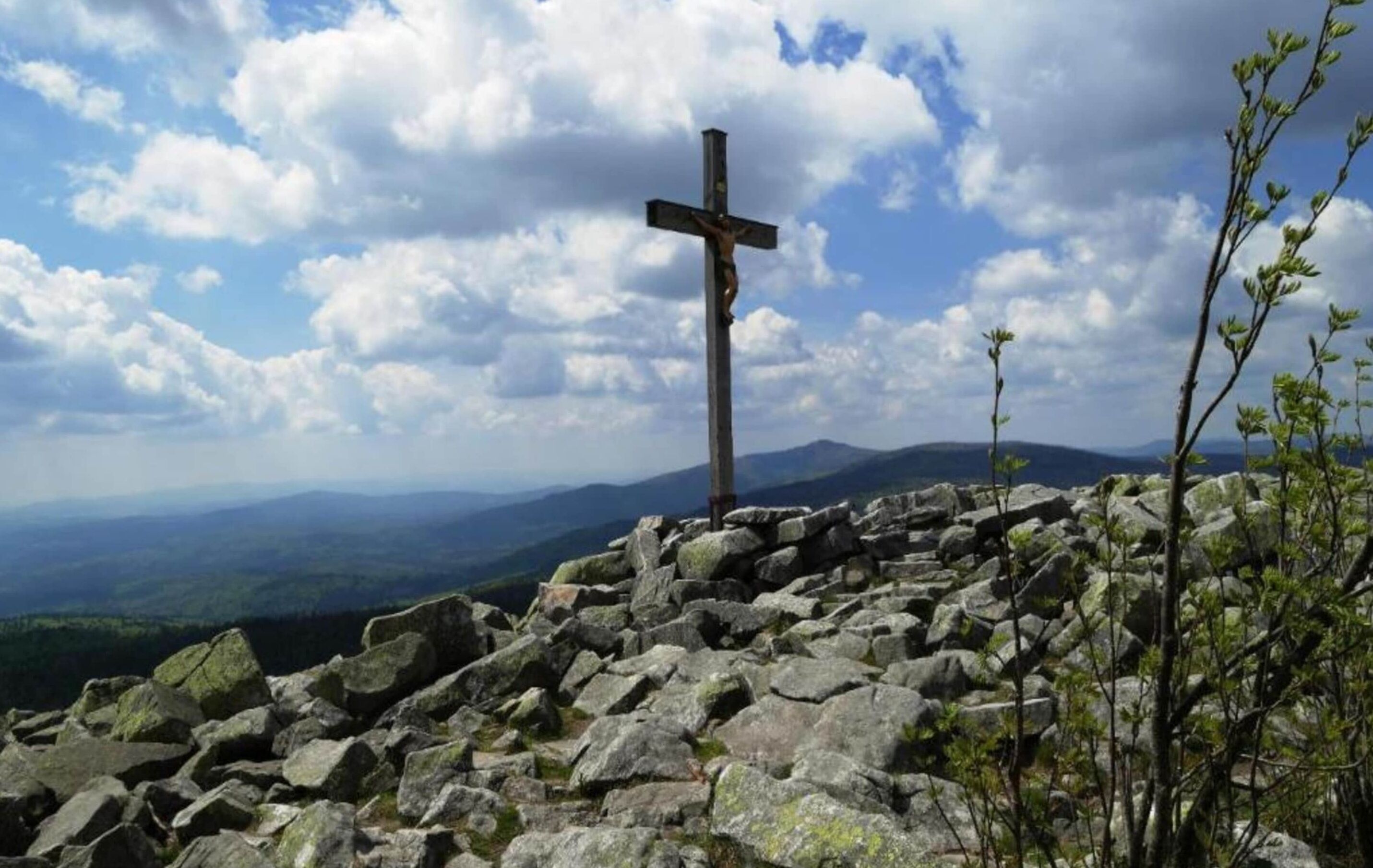 Una cruz sobre un afloramiento rocoso con un paisaje montañoso al fondo.
