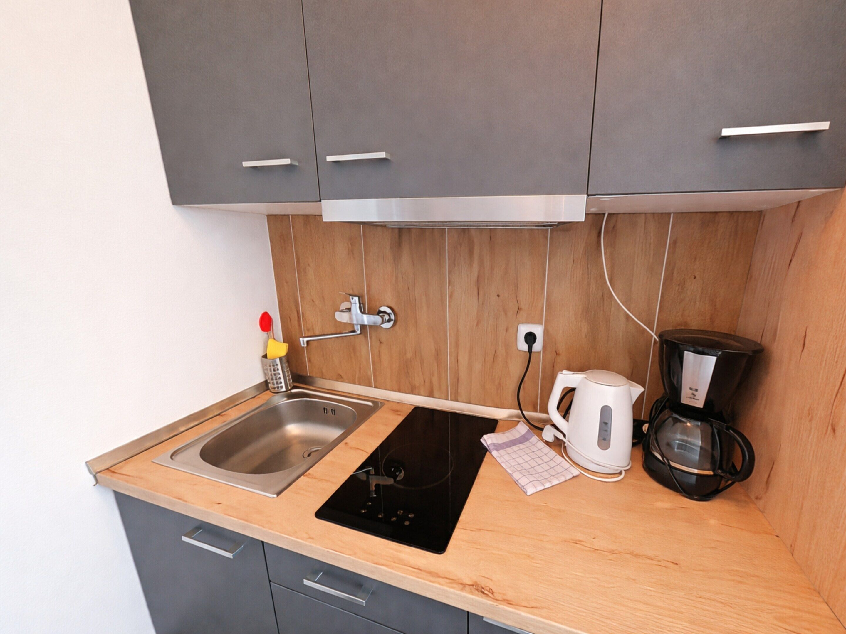 A compact kitchen with a sink, stove, and coffee maker.