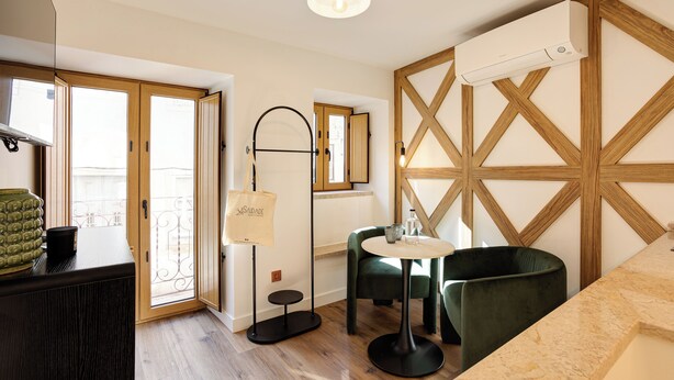 Une pièce moderne avec un plancher en bois, une table ronde, une chaise verte, un ventilateur de plafond et une grande fenêtre.