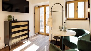 Une chambre moderne dotée d’un téléviseur à écran plat, d’une commode en bois avec des tiroirs, d’une table ronde avec des chaises et d’une grande fenêtre offrant une vue dégagée.