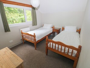 Quarto com duas camas de madeira, uma mesinha de madeira e uma janela com cortinas.