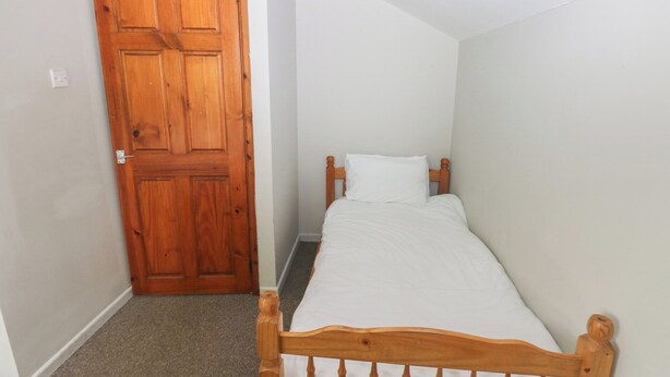 Una habitación pequeña con una cama individual, cabecera de madera, puerta de madera y piso alfombrado.