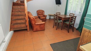 Una habitación con una escalera espiral de madera, sofás de cuero, una mesa de comedor con sillas, un televisor montado en la pared y una ventana con cortinas.