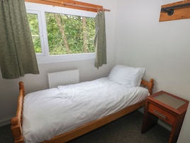 A single bed with white bedding, a wooden headboard, a window with curtains, a radiator, and a small wooden nightstand with a drawer.