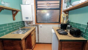Cocina compacta con lavamanos, refrigerador pequeño, ventana con vistas y electrodomésticos básicos.