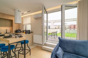 A modern kitchen with a dining area, a sofa, and a view of a garden and buildings. - Dębniki Apt – Terrace, A/C, Parking – by Rentujemy (Kraków)