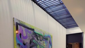Ein Flur mit einem großen abstrakten Gemälde an der Wand, einer Decke mit horizontalen Lamellen und einer Tür zu einem anderen Raum.