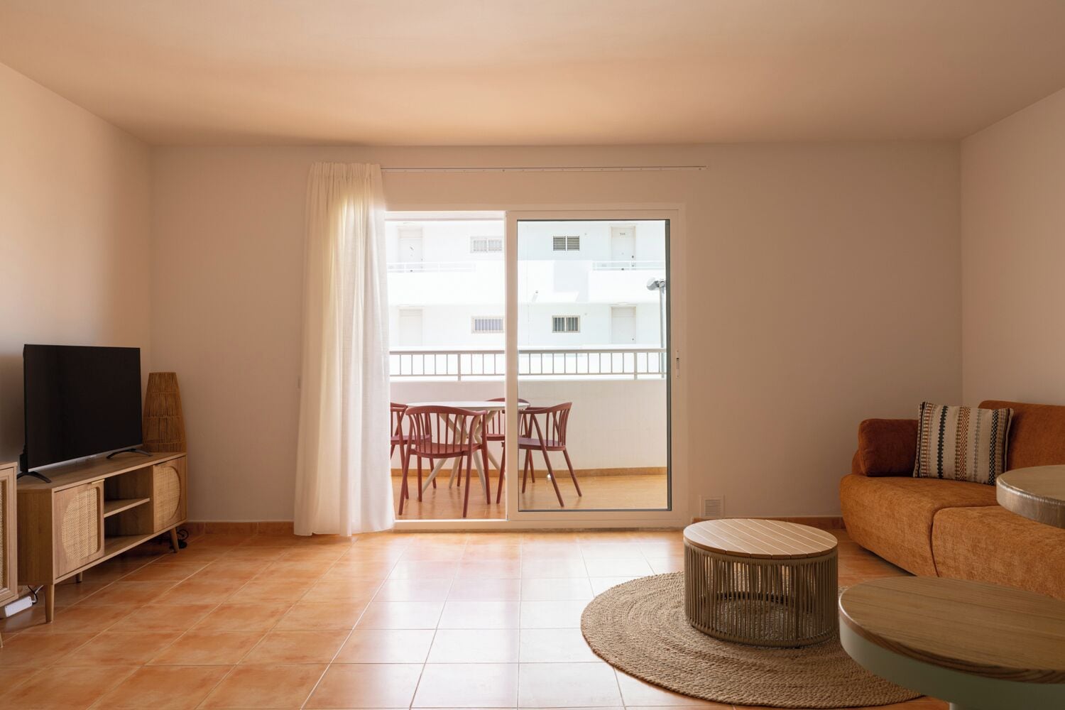 Un salon équipé d’un téléviseur, d’un canapé, d’une table basse ronde et d’un balcon avec des chaises.