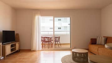 Un salon équipé d’un téléviseur, d’un canapé, d’une table basse ronde et d’un balcon avec des chaises.