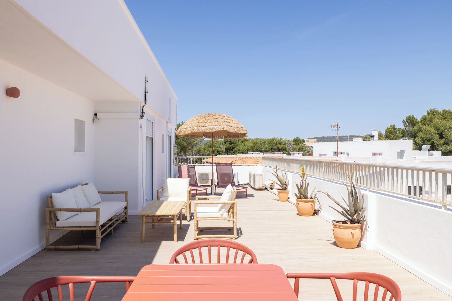 A balcony with a sofa, chairs, a table, potted plants, and a thatched umbrella.