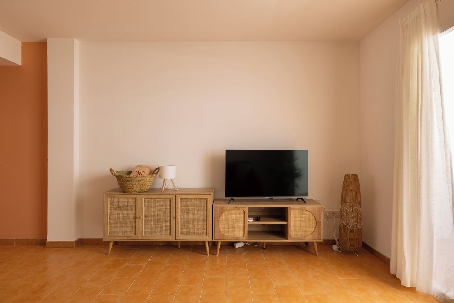 A room with a television on a wooden cabinet, a wicker basket, and a lamp.