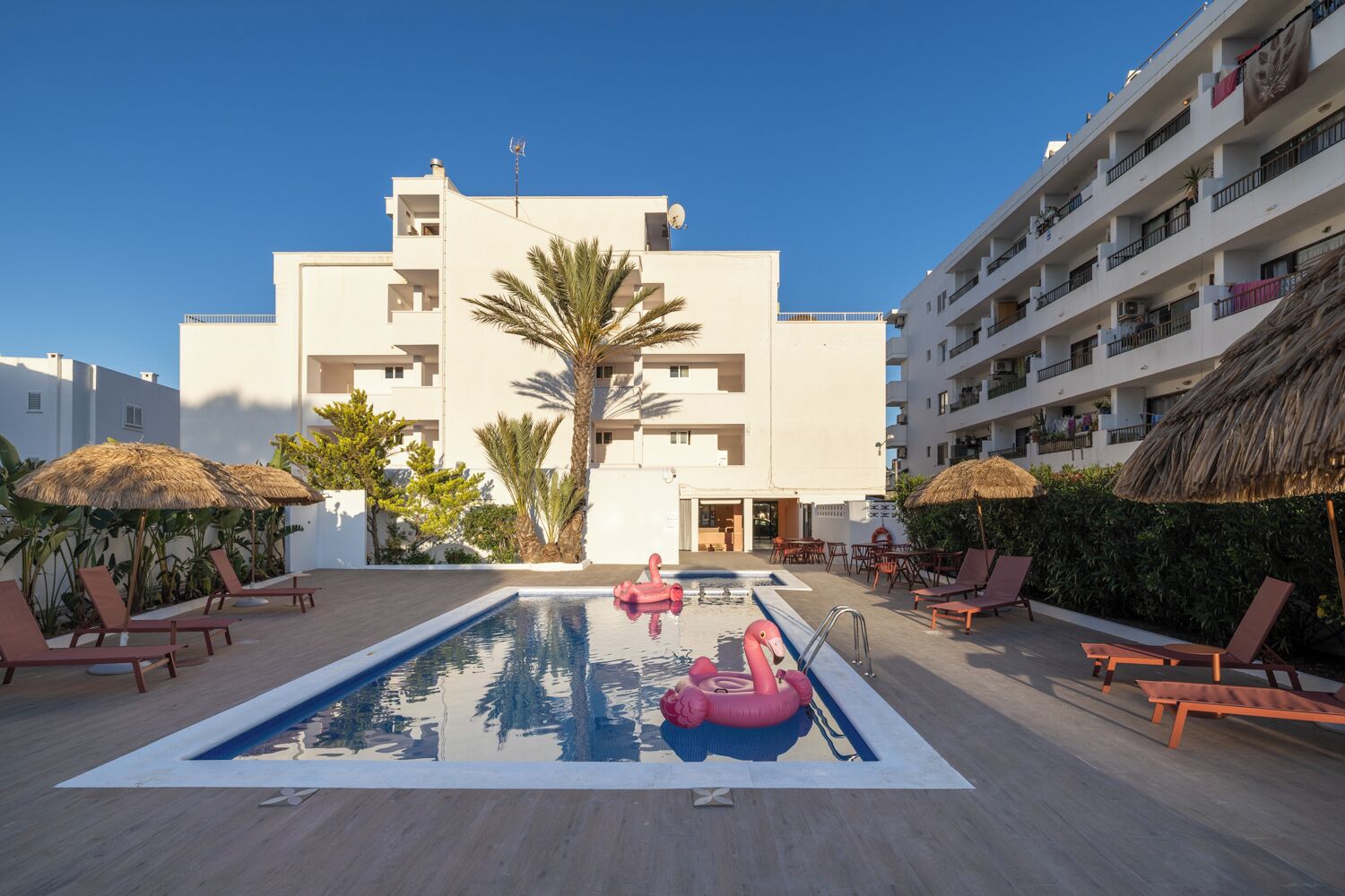 A pool area with lounge chairs, a pool, and a building with balconies.