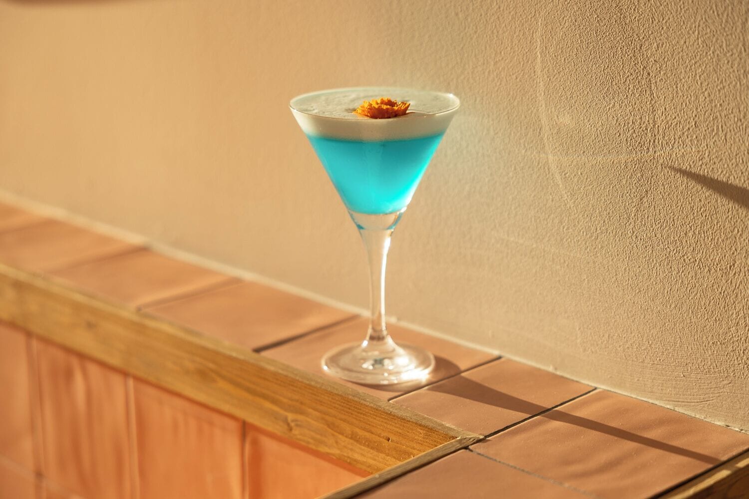 Een martini glas gevuld met een blauwe vloeistof en garnering, op een houten plank.