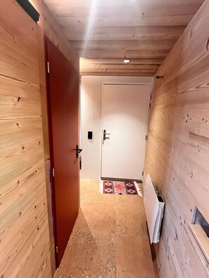 A hallway with wooden walls, a tiled floor, a door, and a radiator.