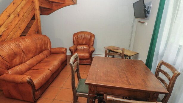 Una habitación con una mesa de madera, dos sillas de madera, un sofá de cuero y otra silla de madera.