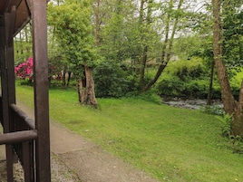 A wooden structure with a pathway leading into a lush green area with trees and a small stream.