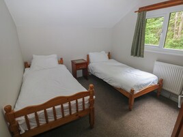 A room with two wooden beds, a small wooden nightstand, a window with a view of greenery, and a radiator.