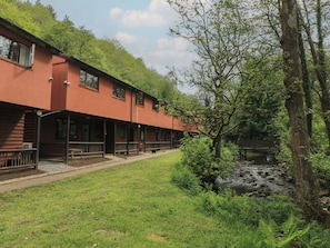 A building with a red exterior, multiple windows, and a covered outdoor area with benches. - Cabin No. 6 - Salt and Fern Cabins (Port Talbot)