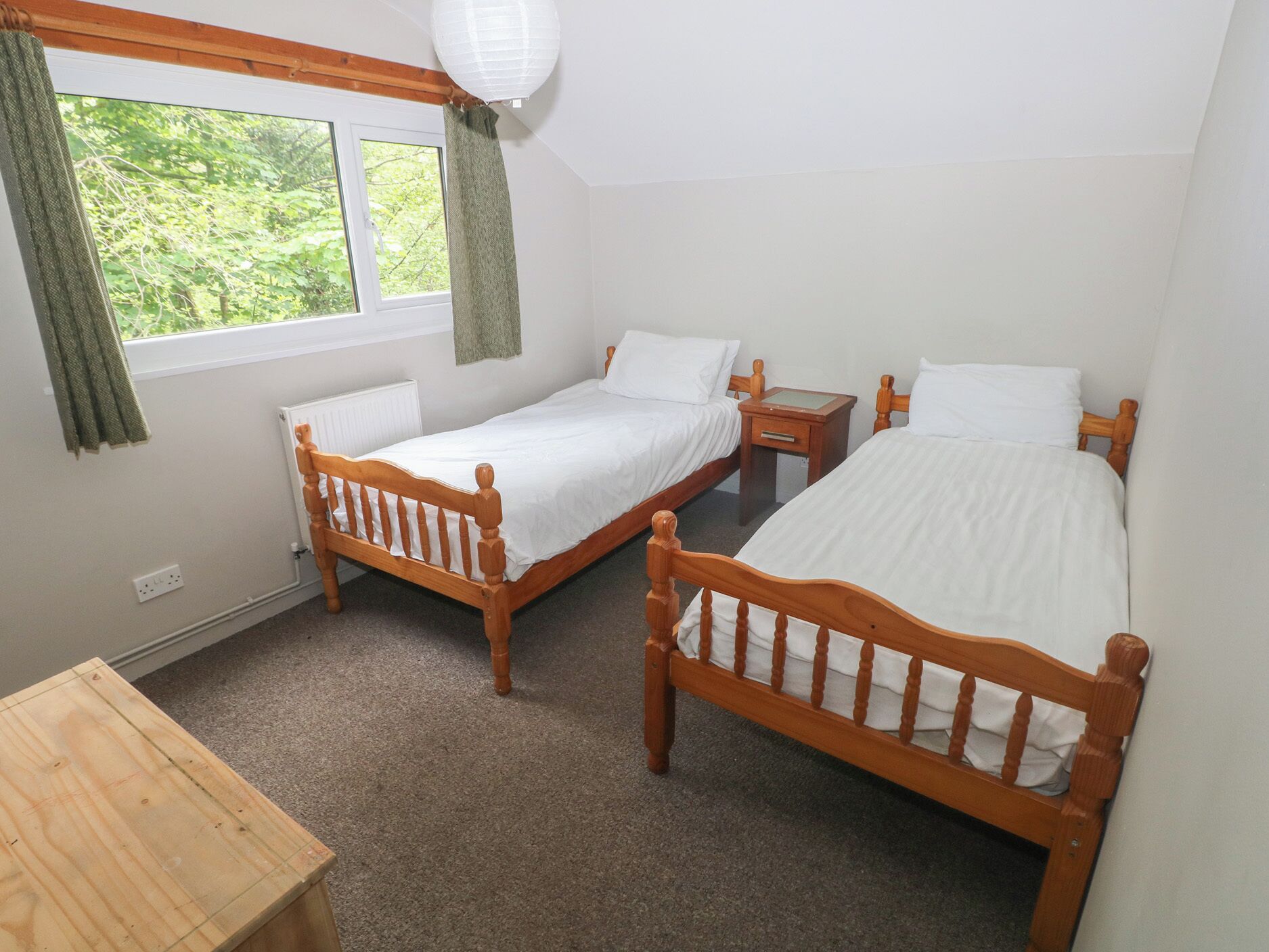 A room with two wooden beds, a small wooden table, and a window with curtains.