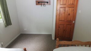 Una habitación con dos camas individuales, una puerta de madera, un perchero y un enchufe en la pared.