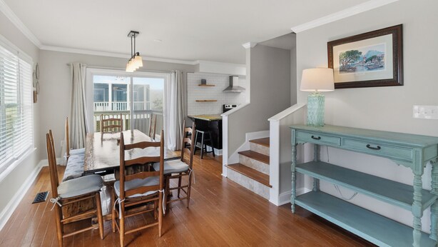 Un comedor con una mesa y sillas de madera, una escalera, una consola azul aguamarina y un cuadro en la pared.