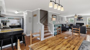 Una cocina moderna con una isla central, una zona de comedor con mesa de madera y una escalera que sube a otro nivel.