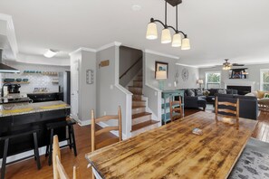 Eine moderne Küche mit einer zentralen Kochinsel, einem Essbereich mit Holztisch und einer Treppe, die eine weitere Ebene hinaufführt.