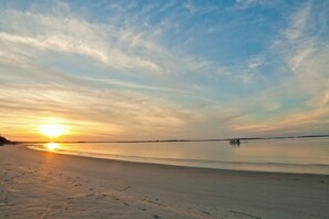 Ein Strand mit Sonnenuntergang, ruhigem Wasser und einem entfernten Boot.