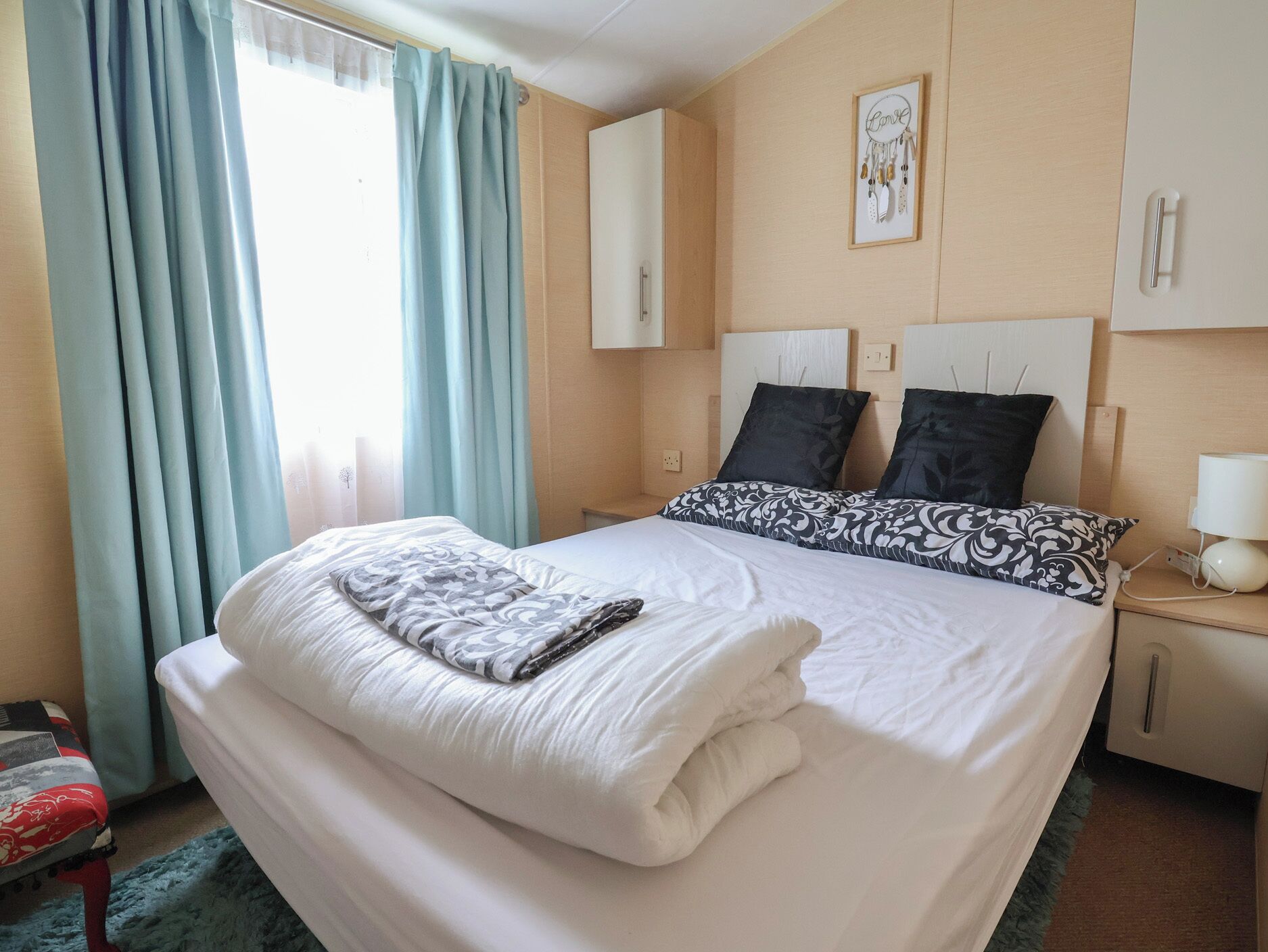 Quarto de hotel com cama, mesa de cabeceira, luminária, janela com cortinas e um quadro na parede.