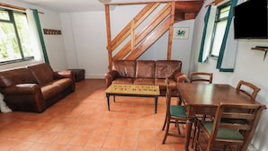 Una sala de estar con una escalera de madera, un sofá de cuero marrón, una mesa de comedor de madera con sillas y un letrero sobre la mesa.